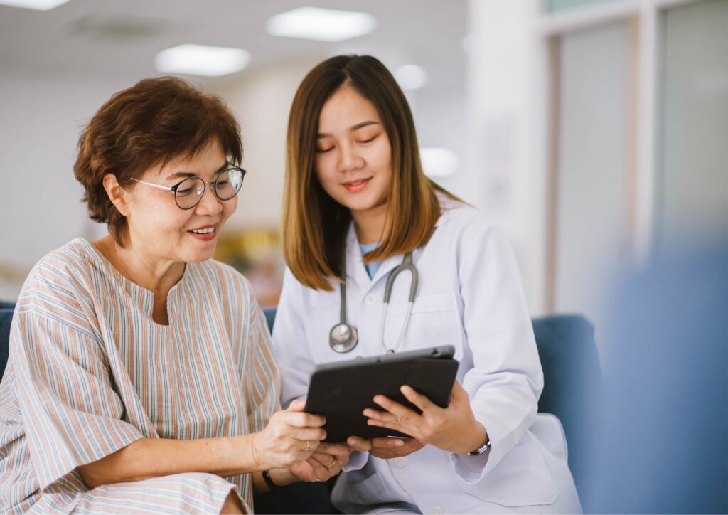 Médica com estetoscópio mostra informações em tablet para paciente idosa, representando comunicação clara e empática na saúde.