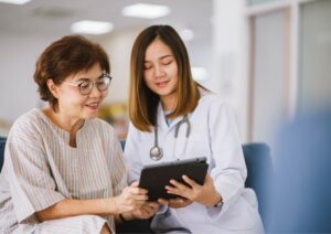 Médica com estetoscópio mostra informações em tablet para paciente idosa, representando comunicação clara e empática na saúde.