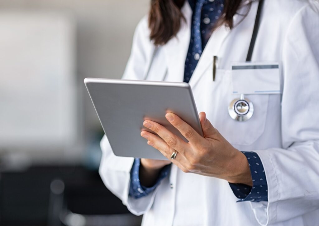 Profissional da saúde usando tablet, com jaleco branco e estetoscópio, representando gestão de marca e presença digital no setor médico.