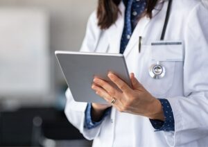 Profissional da saúde usando tablet, com jaleco branco e estetoscópio, representando gestão de marca e presença digital no setor médico.