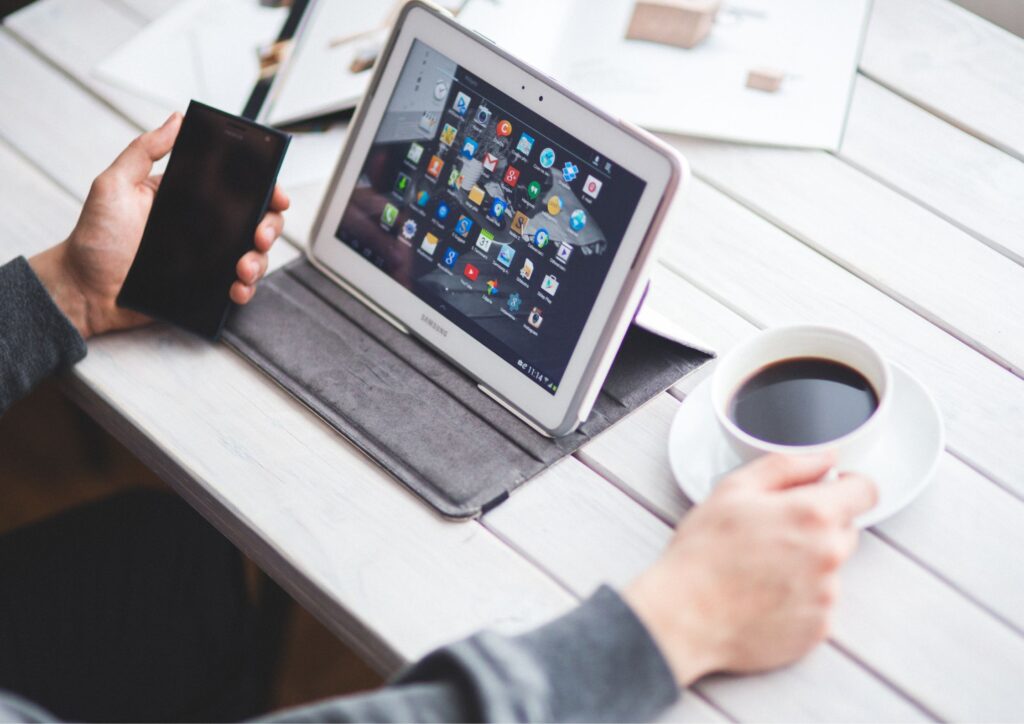 Pessoa utiliza tablet e smartphone ao lado de uma xícara de café, representando conectividade e presença on-line estratégica no setor da saúde.